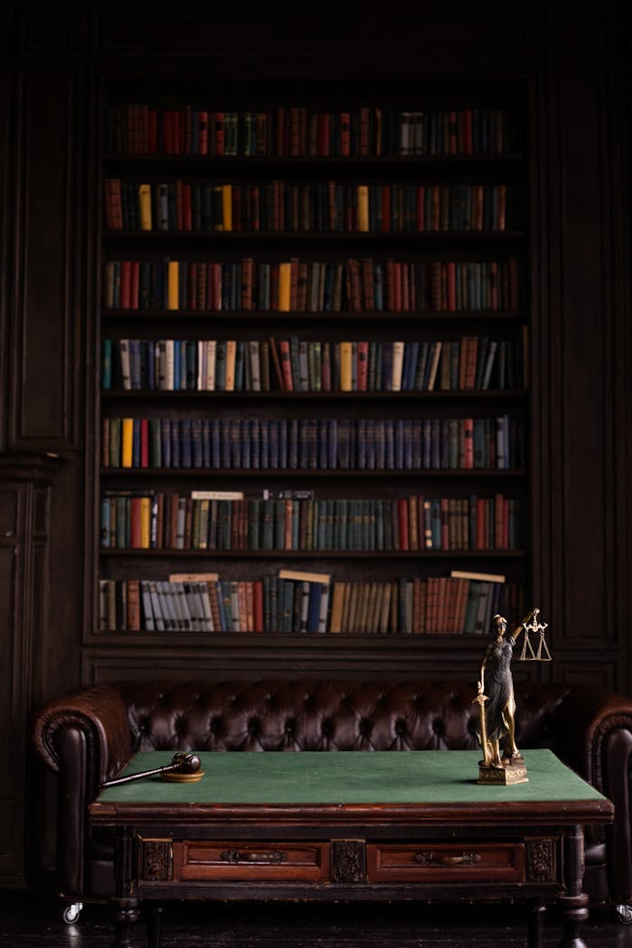A sophisticated library scene featuring a leather sofa, bookshelves, and a statue of justice with a gavel on the table.